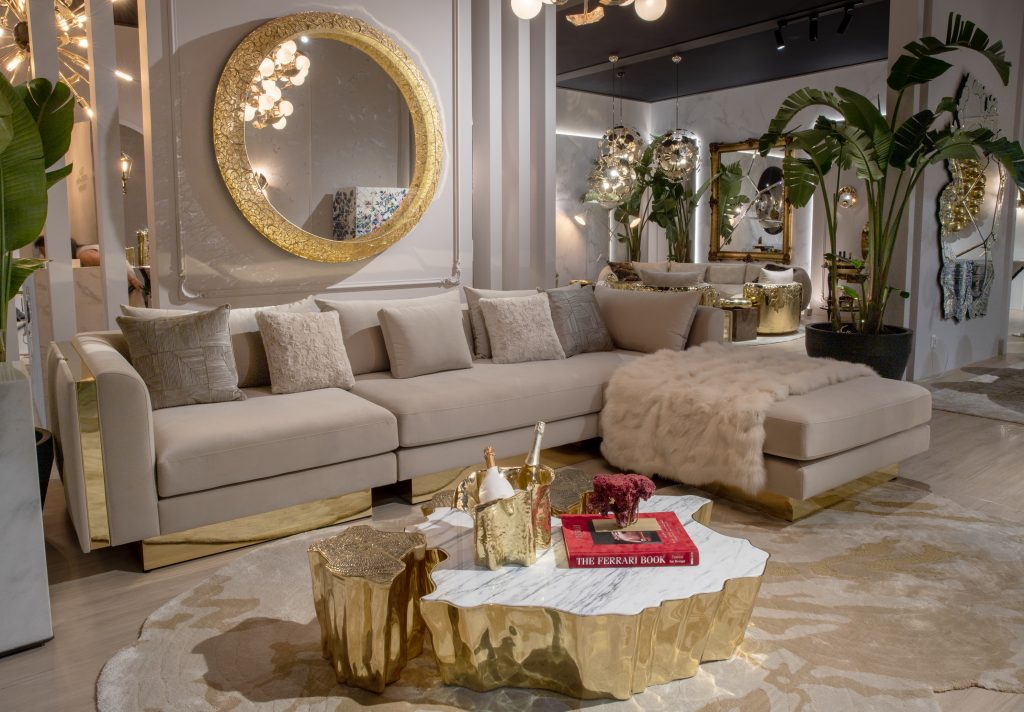 Boca do Lobo- a living room with a big cream sofa , a gold ring mirror, a wood center table and thete's a curved sofa behind , a mirror on the wall and some lamps
